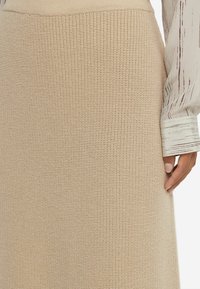 Stickad beige midikjol med ett strukturerat mönster, med en figurnära midja och en slät, mjuk yta. Accenterad av en ljus, mönstrad blus.
