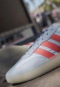 Svijetloplavi cipela s teksturiranim velur i glatkom kožom. Ima tri crvene pruge, okrugli vrh i prozirnu gumenu potplat.