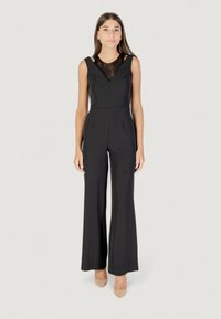 Mono negro con un corsé ajustado, detalles de encaje en el escote y pantalones de pierna ancha. Textura de tejido suave, utilizado con tacones nude.