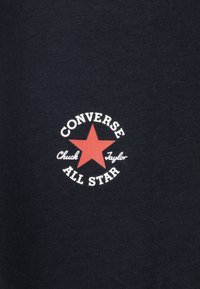 Black fabric shirt featuring a circular logo with a red star, white text stating "CONVERSE," "Chuck Taylor," and "ALL STAR."
