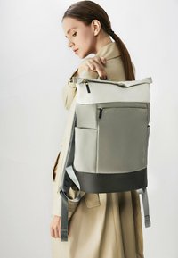 Sac à dos gris et noir avec un design à enroulement, poche latérale et sangles ajustables. Fabriqué en tissu durable avec une texture lisse.