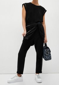 Czarny top z krótkim rękawem i okrągłym dekoltem, w połączeniu z czarnymi, zwężającymi się spodniami z troczkiem. Białe sneakersy i niebieska torba w wzory.