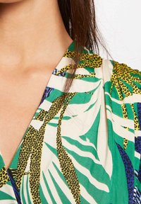 Blusa de manga corta con un patrón de hojas verde, blanco y amarillo y estampado de leopardo, hecha de una tela ligera con un diseño de escote en V.