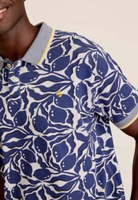Navy en witte polo met een bladdessin, voorzien van een grijze kraag en gele accenten op de mouwen, gemaakt van gestructureerd katoen.