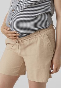 Pantalones cortos de lino beige claro con cintura elástica y cordón, combinados con una camiseta a rayas en azul marino y blanco.