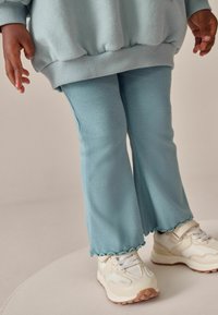 Lysblå, ribbede flared bukser med bølget kant, parret med cremefarvede sneakers med mesh detaljer og strukturerede såler.