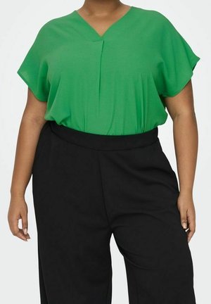 Grüne Bluse mit V-Ausschnitt und kurzen Ärmeln, lockerer Passform, fallendem Stoff und einem dezenten vorderen Falz, kombiniert mit schwarzen, hoch taillierten Hosen.
