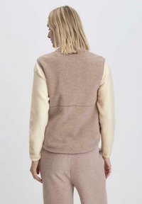 Fleece-Weste in Hellrosa und Creme, mit hohem Kragen, langen Ärmeln und weichem Material. Taillierter Schnitt mit nahtloser Rückenpartie.