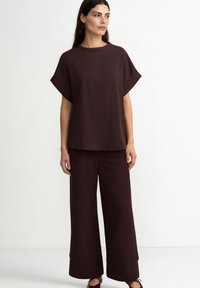 Maroon top with wide sleeves and a round neckline paired with matching loose-fit trousers. Smooth fabric with a subtle sheen.