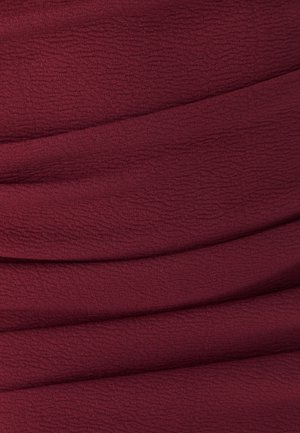 Tessuto borgogna testurizzato con pieghe sottili. La superficie presenta un motivo leggermente stropicciato, creando profondità e interesse visivo.