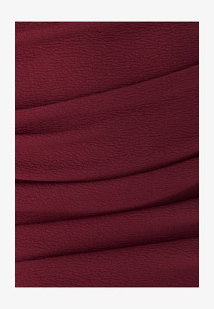 Tessuto borgogna testurizzato con pieghe sottili. La superficie presenta un motivo leggermente stropicciato, creando profondità e interesse visivo.