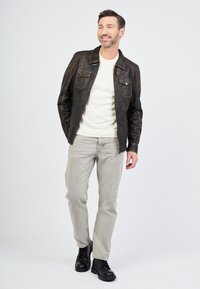 Schwarze Lederjacke mit strukturierten Schultern, cremefarbener Pullover, hellgraue Jeans und schwarze Schnürstiefel. Einfaches, lässiges Outfit.