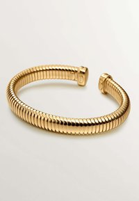 Pulsera de brazalete en tono dorado con un diseño flexible y parecido a un resorte. Superficie suave y pulida con extremos redondeados y segmentos espaciados uniformemente.