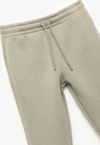 Hellgraue Sweatpants aus weichem Stoff. Verfügt über einen elastischen Bund mit Kordelzug und schmal zulaufenden Beinen. Glatte Textur, keine sichtbaren Muster.