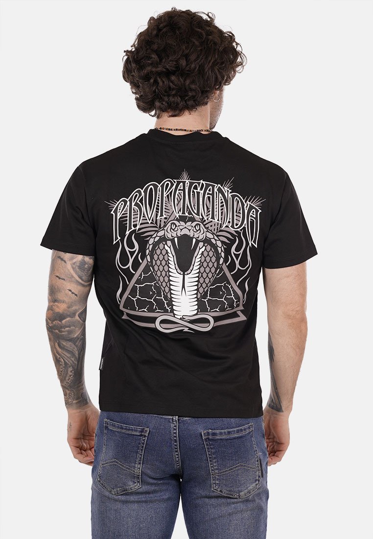 Maglietta nera in cotone con una grande grafica di un cobra e la scritta "PROPAGANDA" in inchiostro bianco sul retro, con una vestibilità casual.