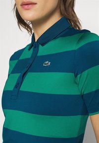 Green and navy striped polo shirt with a collar, features two buttons, and a small Lacoste logo on the left side of the chest.