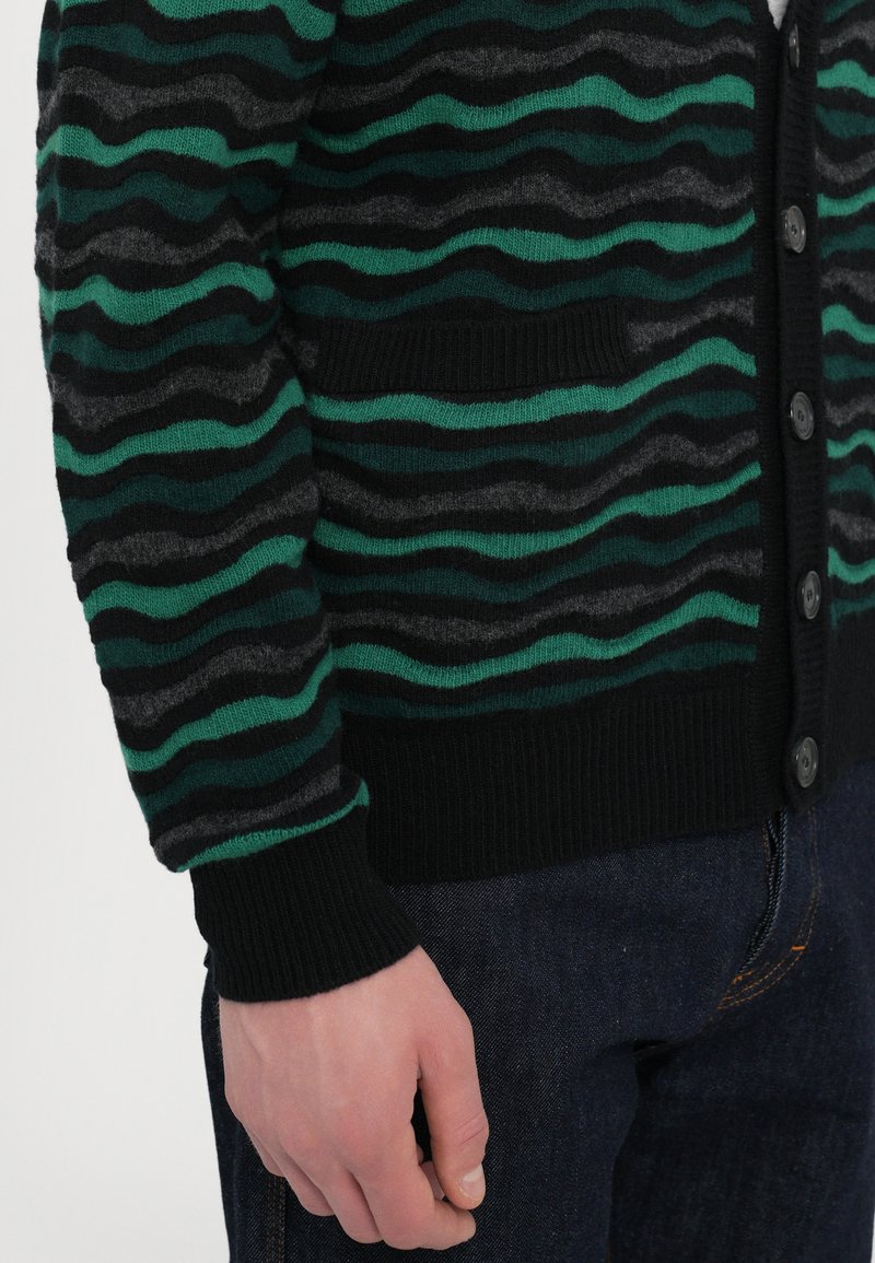 Green and black striped cardigan with wave patterns, featuring a black ribbed hem, button closure, and textured knit material.