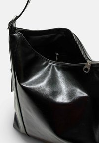 Borsa in pelle nera con chiusura a zip, che mostra una texture liscia e lucida e un interno spazioso. Include un tirazip in metallo e manico.