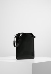 Mustassa kiiltävässä käsilaukussa on suorakulmainen muoto ja hopeanvärinen säädettävä hihna. Laukussa on sileä pinta ja minimalistinen muotoilu.