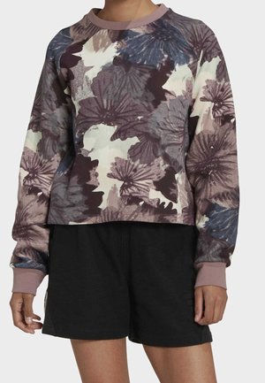 Personne portant un sweat à manches longues à motif floral dans des tons violets sourds et un short de sport noir.