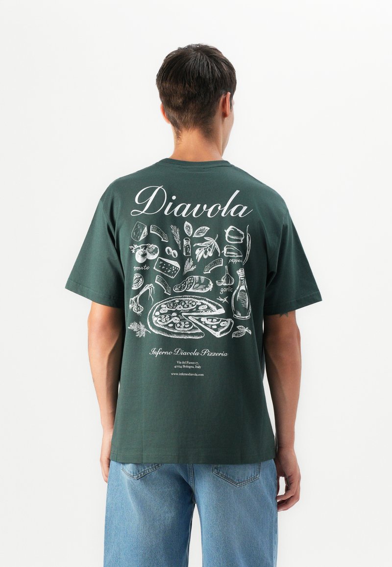 Man wearing dark green t-shirt with white illustrations of pizza, ingredients, and text promoting Inferno Diavola Pizzeria, standing against white background.