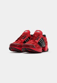 Red athletic shoes with black accents, textured upper, and striped design. Features a cushioned sole and lace-up front for secure fit.