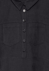 Camicia in corduroy nero con colletto, dotata di sei bottoni e due tasche sul petto. Il tessuto presenta una superficie testurizzata.