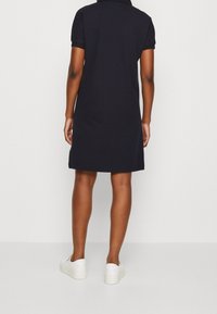 Vestido polo de color navy con mangas cortas, corte recto y cuello. Combinado con zapatos blancos tipo slip-on, con una textura de tela suave.
