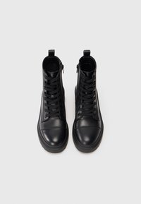 Botas de tobillo de cuero negro con un acabado suave, puntera redonda, cierre de cordones, cremalleras laterales y suelas de goma texturizadas.