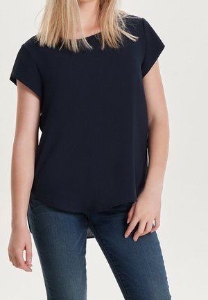 Navyblauwe blouse met korte mouwen en een ronde hals, gemaakt van een gladde stof, met een gebogen zoom en een ontspannen pasvorm. Gecombineerd met een blauwe spijkerbroek.