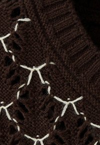 Gros plan sur un tissu tricoté marron foncé avec des détails de couture blancs et de petits trous dans un motif texturé.