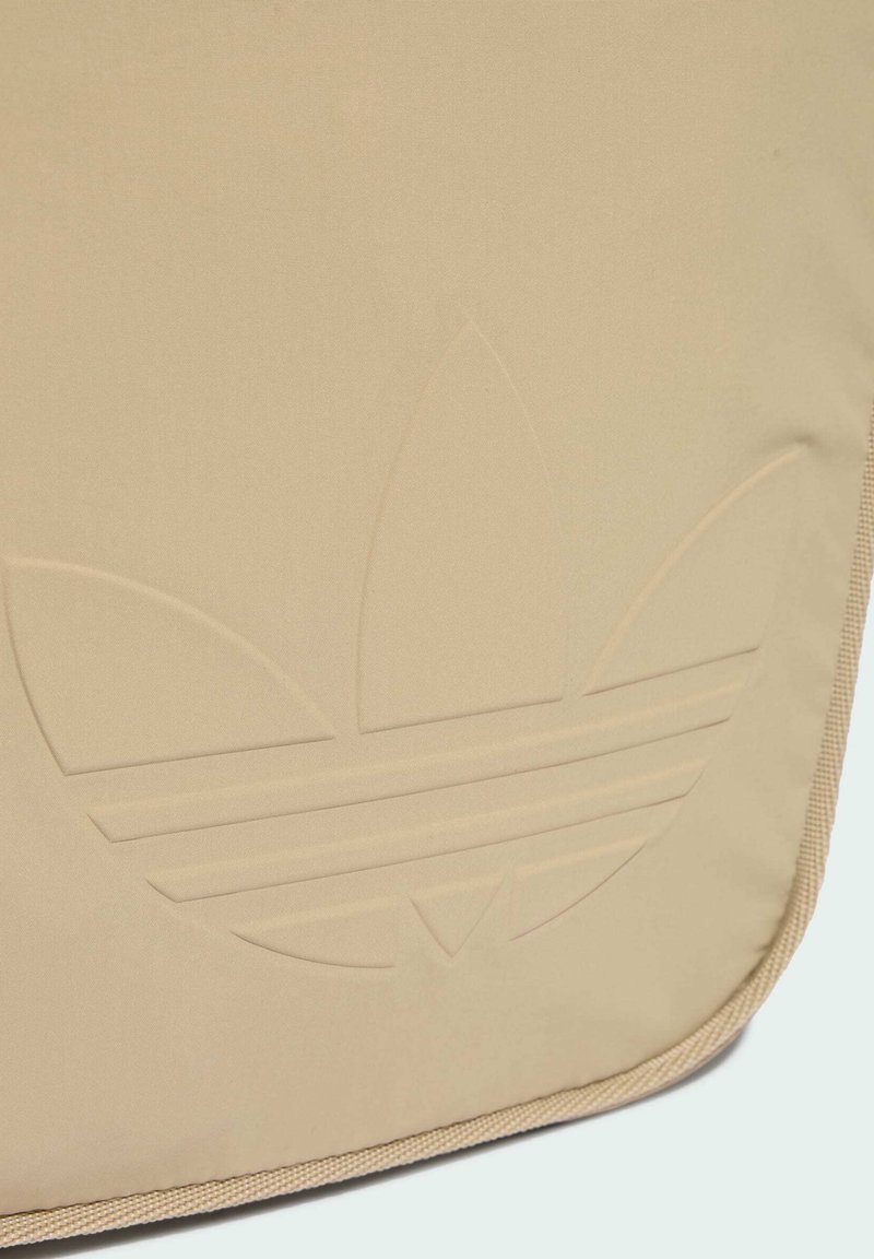 Beige Stofftasche mit einem geprägten Logo, das drei Streifen und ein Kleeblatt-Design zeigt, eingefasst mit einem strukturierten, hellbraunen Rand.