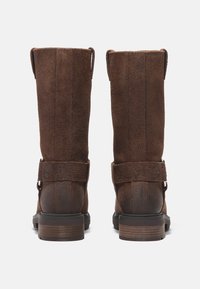 Hnědé semišové boty s vysokým kotníkem, ozdobnými popruhy a středním dřevěným podpatkem, se strukturovaným povrchem a zpevněnými švy.