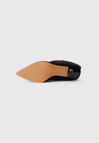Black suede heel with a pointed toe, featuring a smooth black patent leather accent on the heel and a textured tan rubber sole.