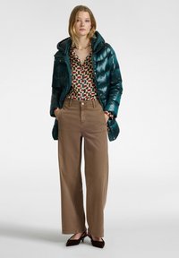 Tyrkysová péřová bunda, vzorovaná blůza s geometrickým designem, béžové široké kalhoty a hnědé podpatky. Hladká textura a lesklý povrch bundy.