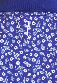 Blå mönstrad tyg med små vita blommor och blad, med en texturerad midjeband. Inkluderar subtila sömnadsdetaljer.