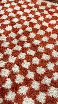 Tapis texturé à carreaux rouges et blancs avec un motif en relief et duveteux sur un sol en bois.