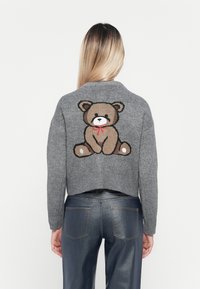 Maglione grigio a maglia con design corto, caratterizzato da una grafica di un orso bruno con un fiocco rosso sul retro. Tessuto morbido e bordi a coste.