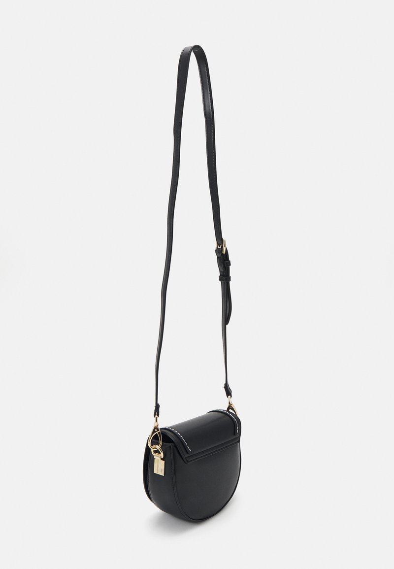 Borsa a tracolla nera in pelle con forma curvata, dettagli in metallo dorato e tracolla slim regolabile. Presenta dettagli di cucitura e una serratura.