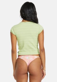 Haut à manches courtes vert rayé avec un design ajusté, associé à un bas de bikini à motif floral rose. Textures et détails du tissu visibles.