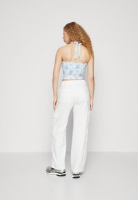 Lys blå blomstrete crop topp med knyting bak, kombinert med hvite vide cargo bukser og grå sneakers. Glatt tekstur, avslappet passform.