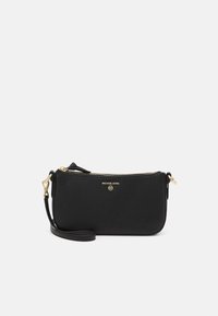 Pochette bracelet Michael Kors en cuir noir avec fermeture éclair dorée et logo, forme rectangulaire fine avec bandoulière amovible sur fond gris clair.