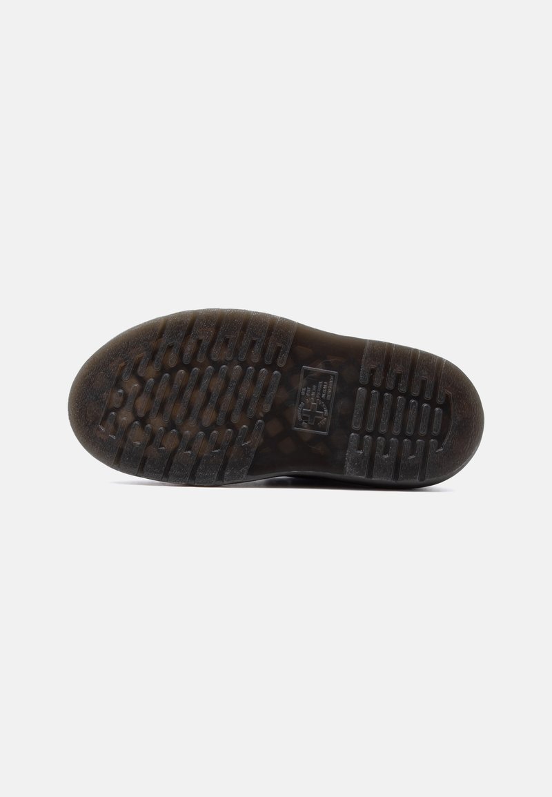 Suola di una scarpa marrone scuro con profonde scanalature a motivo e un piccolo logo rettangolare al centro su sfondo bianco.