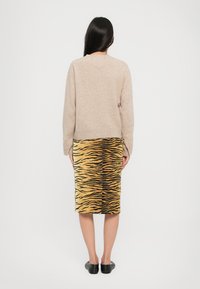 Maglione beige lavorato a maglia con maniche lunghe abbinato a una gonna gialla al ginocchio con un motivo a strisce di tigre nere. Calzature nere.