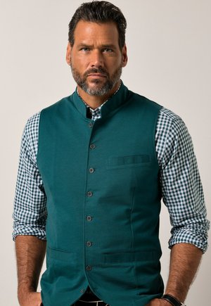 Chaleco sin mangas de color verde azulado con un alto cuello, cierre frontal de botones y un bolsillo en el pecho, superpuesto a una camisa de cuadros verdes y blancos de manga larga.