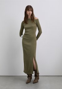 Olivgrön ribbstickad långärmad klänning med axelbandslös halsringning och sidosprund, kombinerad med bruna boots med rynkad design vid ankeln.