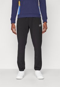 Svart joggebukse med sidelommer, innsvingt design og logodetalj. Kombinert med hvite joggesko for et komplett atletisk utseende.