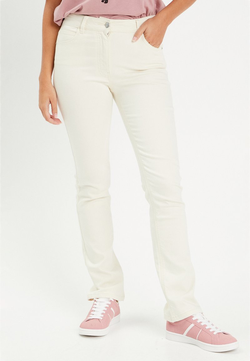 Jeans bianchi a gamba dritta con tasche frontali e zip, abbinati a sneaker rosa con lacci bianchi e suole in gomma.