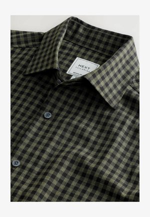 Camisa de cuadros verde y negra con una textura suave, cuello extendido y botones grises; cuenta con una etiqueta que la marca como "NEXT Tailoring."