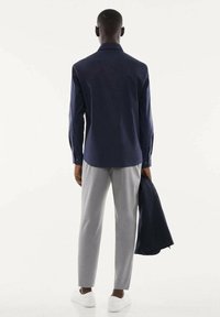Camicia azzurra a maniche lunghe abbinata a pantaloni grigi chiari. La camicia presenta un colletto standard e polsini a bottoni, con una texture liscia, indossata con una giacca.